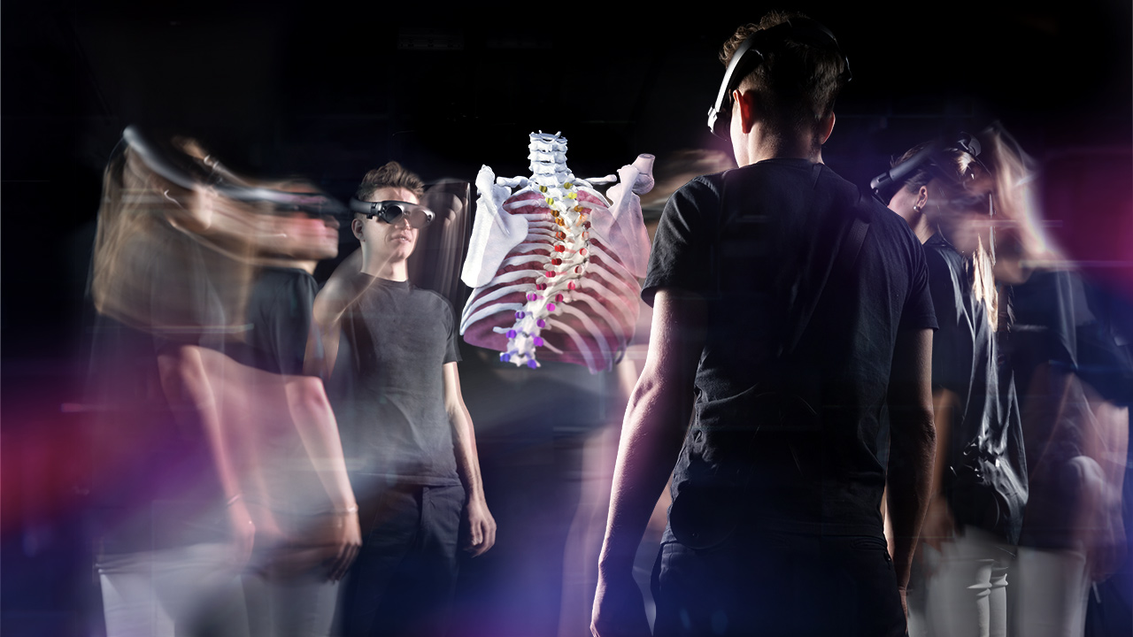 Three people wearing augmented reality glasses move around the digitally projected image of the bones of a human torso