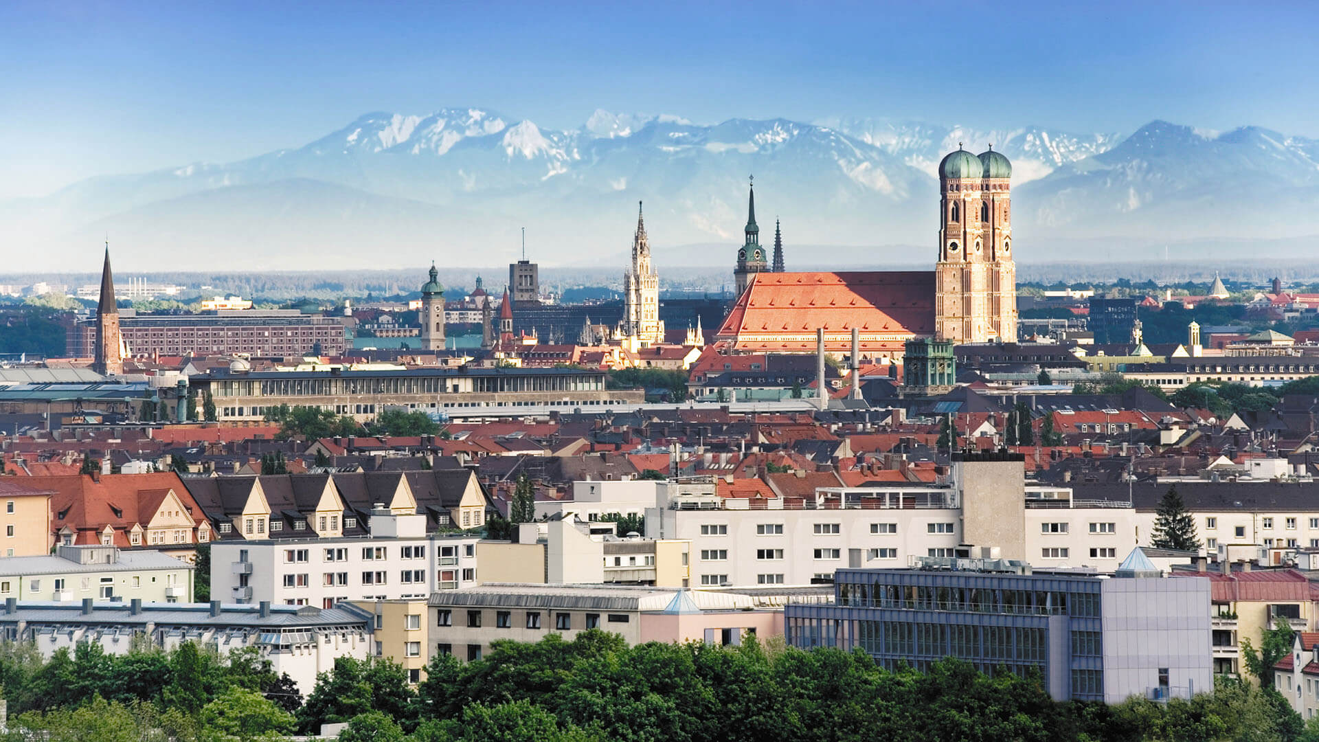 Scenic view of Munich cityscape with iconic landmarks and distant mountains.