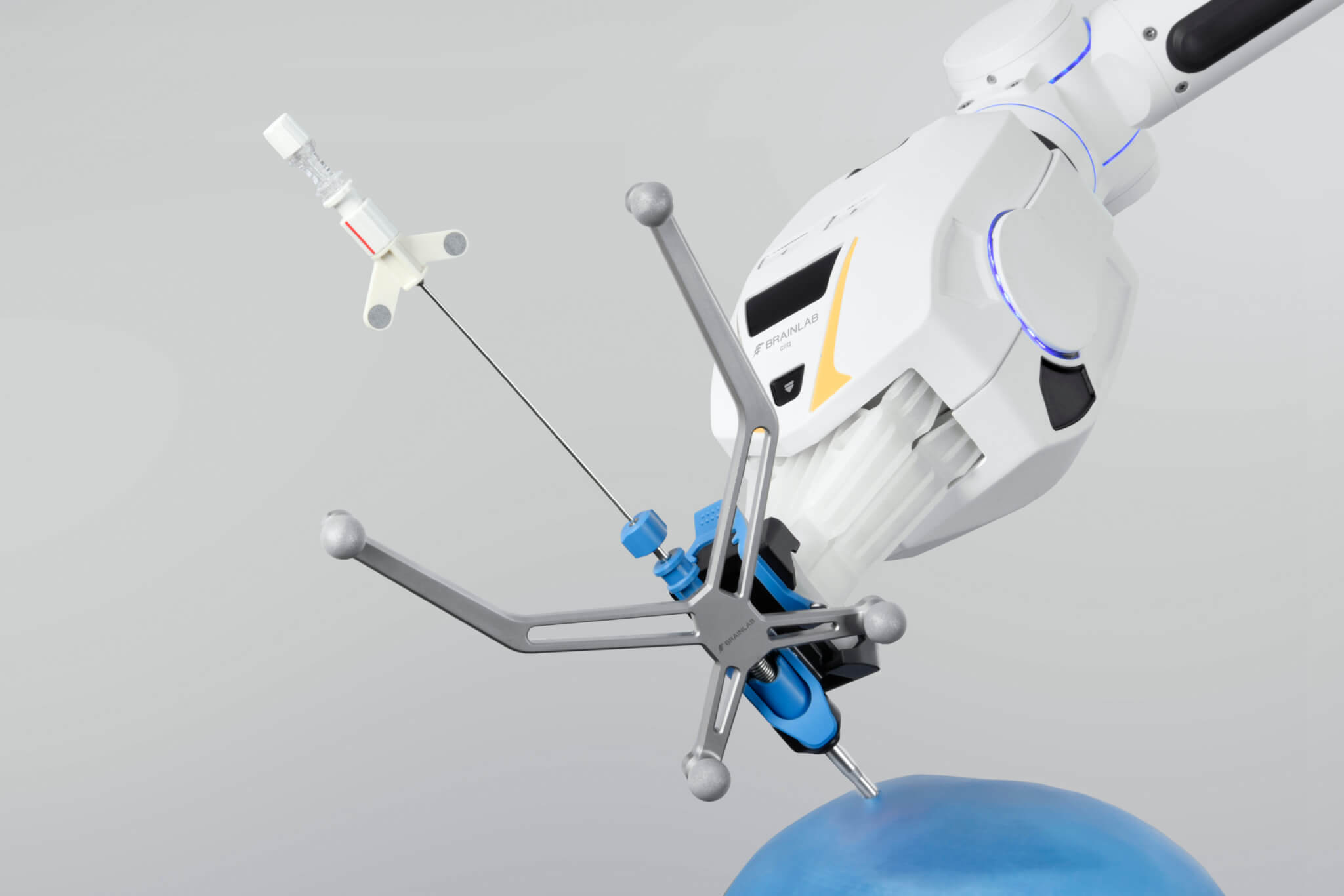 O módulo para cirurgia de crânio de um sistema de braço cirúrgico robótico segura uma agulha de biópsia navegada enquanto paira sobre uma representação azul de um crânio à frente de um plano de fundo cinza